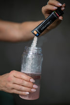 Person pouring creatine powder from a supplement container into a clear bottle against a dark background